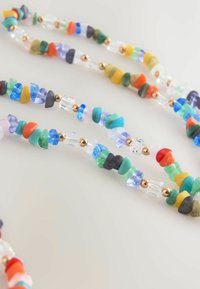Colorful beaded necklace featuring irregular-shaped glass and ceramic beads in various colors, interspersed with gold-tone accents.