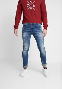 Siniset farkut slim fit -leikkauksella, joissa on kevyitä kulutuksia ja käännetyt lahkeet, yhdistettynä punaiseen college-paitaan, jossa on valkoinen graafinen printti.