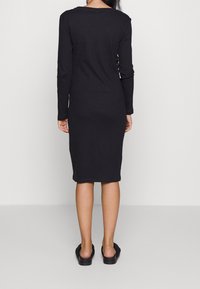 Zwart geribbeld langslijve jurk met een midi-lengte, voorzien van een fitted silhouet en een ronde halslijn. Gepaard met zwarte instappers.