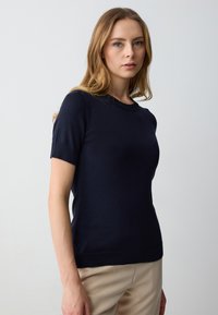 Pullover a maniche corte di un blu navy scuro con scollo rotondo e polsini a coste, caratterizzato da una texture liscia e un design aderente.