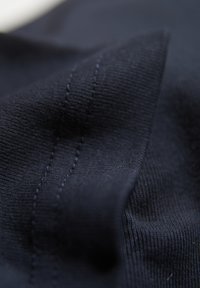 Granatowy materiał o gładkiej fakturze, z delikatnym żebrowaniem i kontrastowym przeszyciem. Zbliżenie ujawnia miękkie szczegóły wzoru tkaniny.