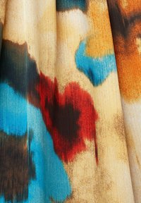 Tissu avec des taches floues abstraites en rouge, bleu, orange, marron et beige, présentant des plis doux et une texture.
