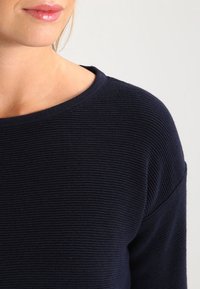 Maglione a coste blu navy con scollo rotondo e motivo testurizzato. Tessuto morbido che appare leggermente oversize, evidenziando un design casual.