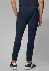 Tmavě modré tepláky z měkké látky, s úzkým střihem, červenými bočními pruhy a detailem zadní kapsy. Nosit je lze se stylovými teniskami.