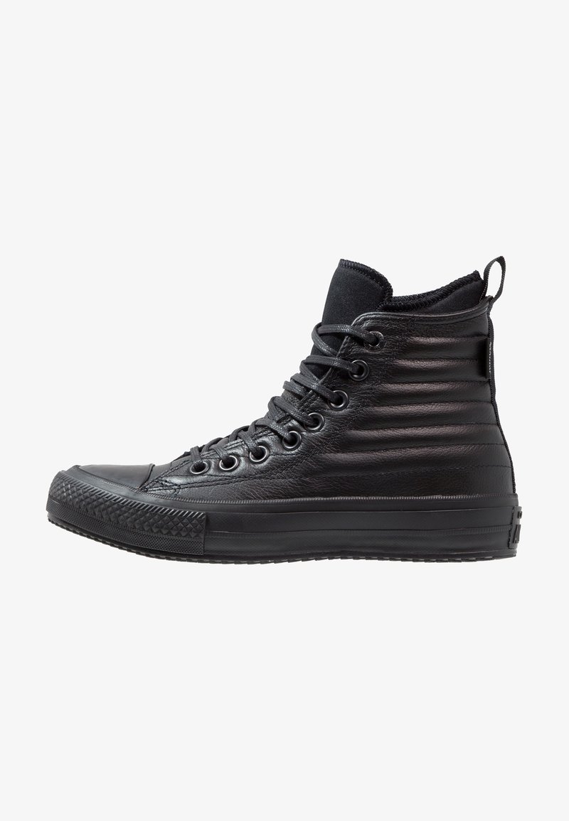 Baskets montantes en cuir noir avec panneaux latéraux matelassés, semelle en caoutchouc noir et lacets noirs sur fond blanc.