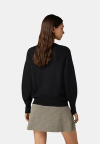 Maglione nero lavorato a maglia con scollo rotondo e maniche voluminose, abbinato a una gonna corta a quadri grigi con texture.
