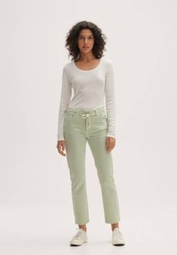 Maglietta bianca a maniche lunghe abbinata a pantaloni dritti verde chiaro con vita regolabile e chiusura a bottone. Indossati con sneakers bianche.