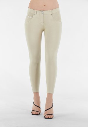 Jeans beige aderenti con vita alta, due tasche frontali e dettagli in metallo argentato. Abbinati a sandali neri con tacco alto e cinghie.