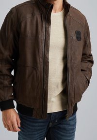 Giacca in pelle marrone con chiusura a zip, polsini a coste e due tasche frontali. Presenta una finitura testurizzata e una patch sul lato sinistro del petto.