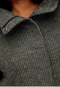 Wollen mix jas in zwart en grijs hounds-tooth patroon, met een hoge kraag en drukknopen, afgewerkt met een gestructureerde look.