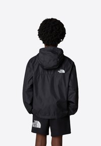 Svart, lättviktsjacka med huva och avslappnad passform, med en liten vit logotyp på övre ryggen. Bärs över matchande svarta shorts.