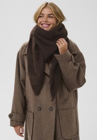 Brun tørklæde lavet af blødt, struktureret stof, draperet om halsen. Matchet med en uldne brun frakke med store lommer og knapper.