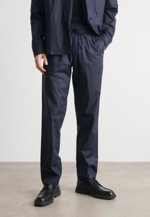 Marineblauwe, lichte broek met een elastische tailleband en een relaxte pasvorm, gecombineerd met zwarte leren schoenen en een bijpassend top.