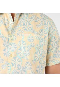 Chemise à manches courtes en lin jaune pâle avec un motif floral bleu. Dotée d'une poche poitrine et de deux boutons.