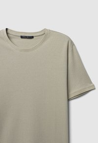 T-shirt corto a maniche corte color beige chiaro in tessuto testurizzato, con scollatura rotonda e orli cuciti, caratterizzato da un design semplice e minimalista.