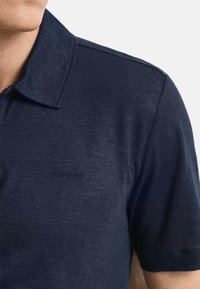 Polo bleu marine en tissu texturé, avec un col à revers et un détail de logo discret. Manches courtes avec une coupe nette.