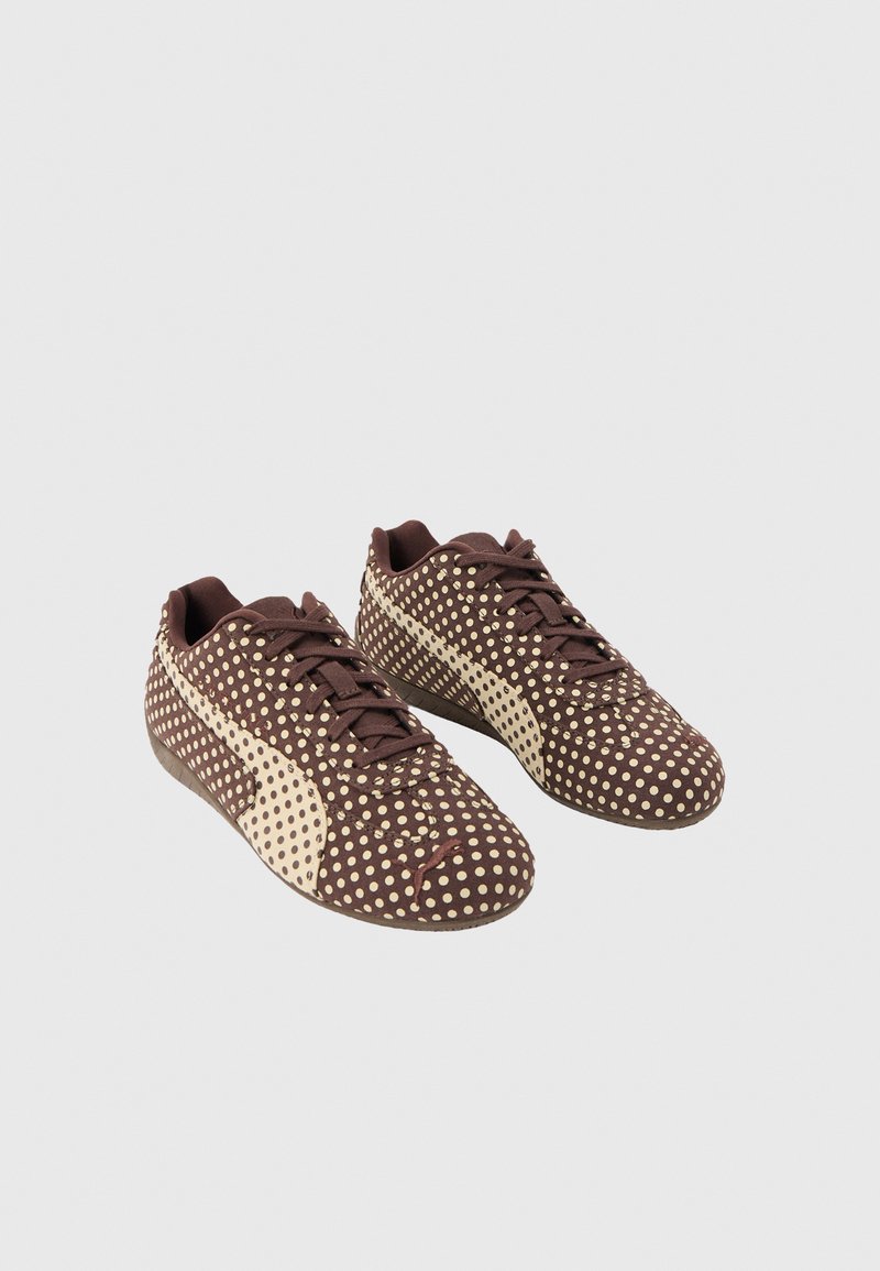 Paire de baskets marron avec des pois beiges et le logo Puma beige sur les côtés, lacées, présentées sur fond blanc.