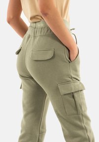 Pantalones cargo de color verde oliva, confeccionados con una tela suave, que cuentan con bolsillos laterales, un corte relajado y una cintura con cordón y detalles de logo.