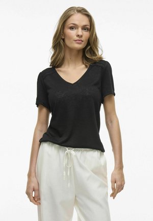 Zwarte V-hals t-shirt met korte mouwen, voorzien van textuurelementen op de schouders. Gekaapt met lichtgekleurde joggingbroek met koord.