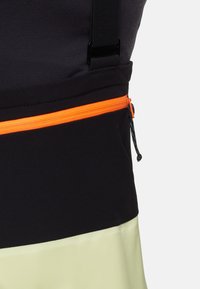 Svart atletisk topp med en orange zippered ficka och justerbara remmar; slät textur med en kontrasterande ljusgrön nederdel.