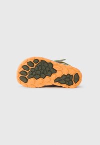 Såle av sko har et teksturert mønster med hexagonale grep i grønt og oransje. Basen er hovedsakelig oransje med detaljer i mørkegrønt.