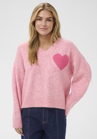 Pull rose tricoté avec un col en V et un ourlet côtelé. Présente un design cœur duveteux rose foncé sur le côté gauche, mettant en valeur une texture douce.