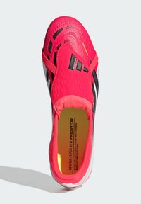 Φωτεινό κόκκινο και μαύρο ποδοσφαιρικό παπούτσι με λευκή σόλα, ελαστικό λουράκι και κίτρινο κείμενο στο πέλμα που αναγράφει «Νέοι Κανόνες για τον Νέο Δράκο».