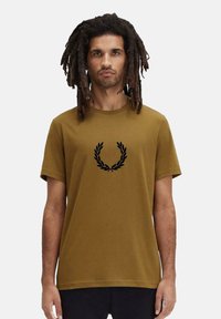 T-shirt di cotone marrone con scollatura a girocollo, caratterizzato da una grafica di una corona d'alloro nera sul petto e maniche corte.