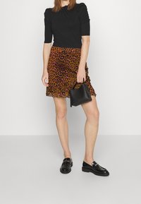 Musta vartaloa myötäilevä toppi, jossa on lyhyet hihat, yhdistetty ruskeaan ja vaaleanpunaiseen leopardikuvioiseen röyhelöhameeseen. Malli pitää kädessään pientä mustaa käsilaukkua. Mustat kengät.