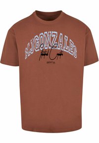 Brown cotton t-shirt with short sleeves, featuring "MJGONZALES" in arching blue text and a black signature graphic. Rounded neck design.
