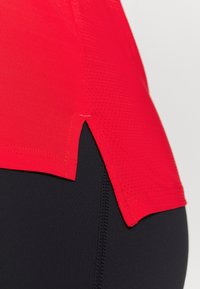 Rode sporttop heeft een textuurdesign en zijkleppen, gecombineerd met zwarte, strakke leggings. Gladde stof met zichtbare stiksels.