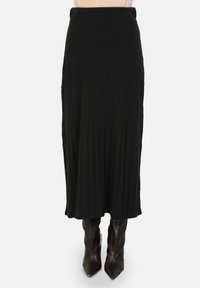 Jupe midi noir à côtes avec une taille cintrée, présentant des plis verticaux et une texture lisse, associée à des bottes pointues montant jusqu'aux genoux.