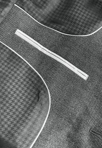 Detail látky s kontrastnými vzormi pepita a tvíd, oddelenými bielym lemom a úzkym horizontálnym otvorom vrecka.