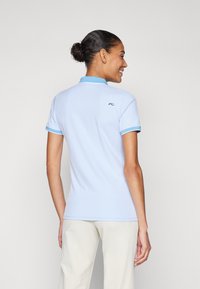 Jasnoniebieska koszulka polo z krótkim rękawem, z fakturowanej tkaniny, z kontrastowym kołnierzykiem i małym logo z tyłu. Prosty, dopasowany krój.