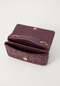 Burgundy läderhandväska med präglad logotypdesign, detaljer i guld, klaffstängning och en rymlig insida med svart foder.