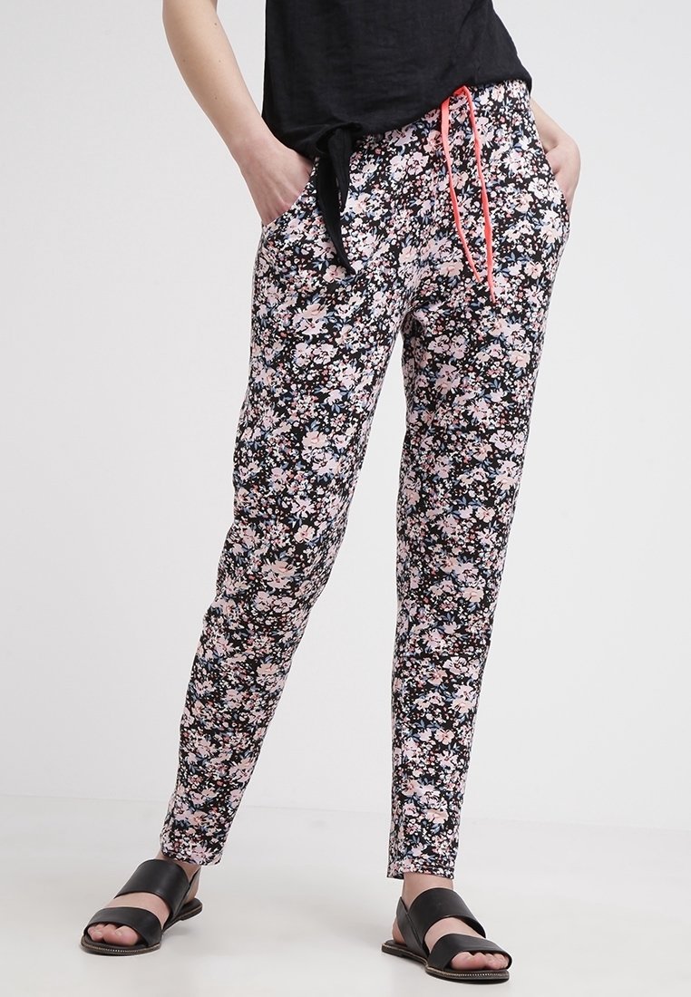 Pantalones con patrón floral sobre un fondo negro, con flores rosas y blancas, cintura elástica y cordón ajustable en naranja neón.