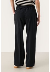 Pantalons larges noirs avec une taille élastique, dotés de deux poches arrière et d'une texture lisse. Portés avec une chemise rayée.