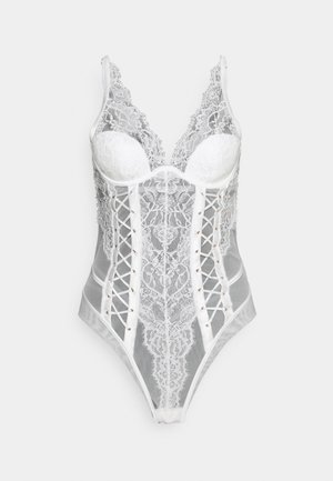 Bijeli čipkasti bodi s podstavljenim čašama, dubokim V izrezom i detaljem vezivanja sprijeda. Ima prozirnu tkaninu i dekorativne gumbe uz strane.