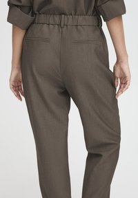 Hose aus braunem, gewebtem Stoff mit lockerem Schnitt, elastischem Bund und zwei Gesäßtaschen, die schmale Nähte aufweisen und keine sichtbaren Verzierungen haben.