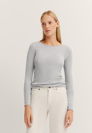 Helles graues Langarmshirt aus weichem Stoff, mit rundem Ausschnitt und tailliertem Schnitt, kombiniert mit weißen Jeans für einen Kontrast.