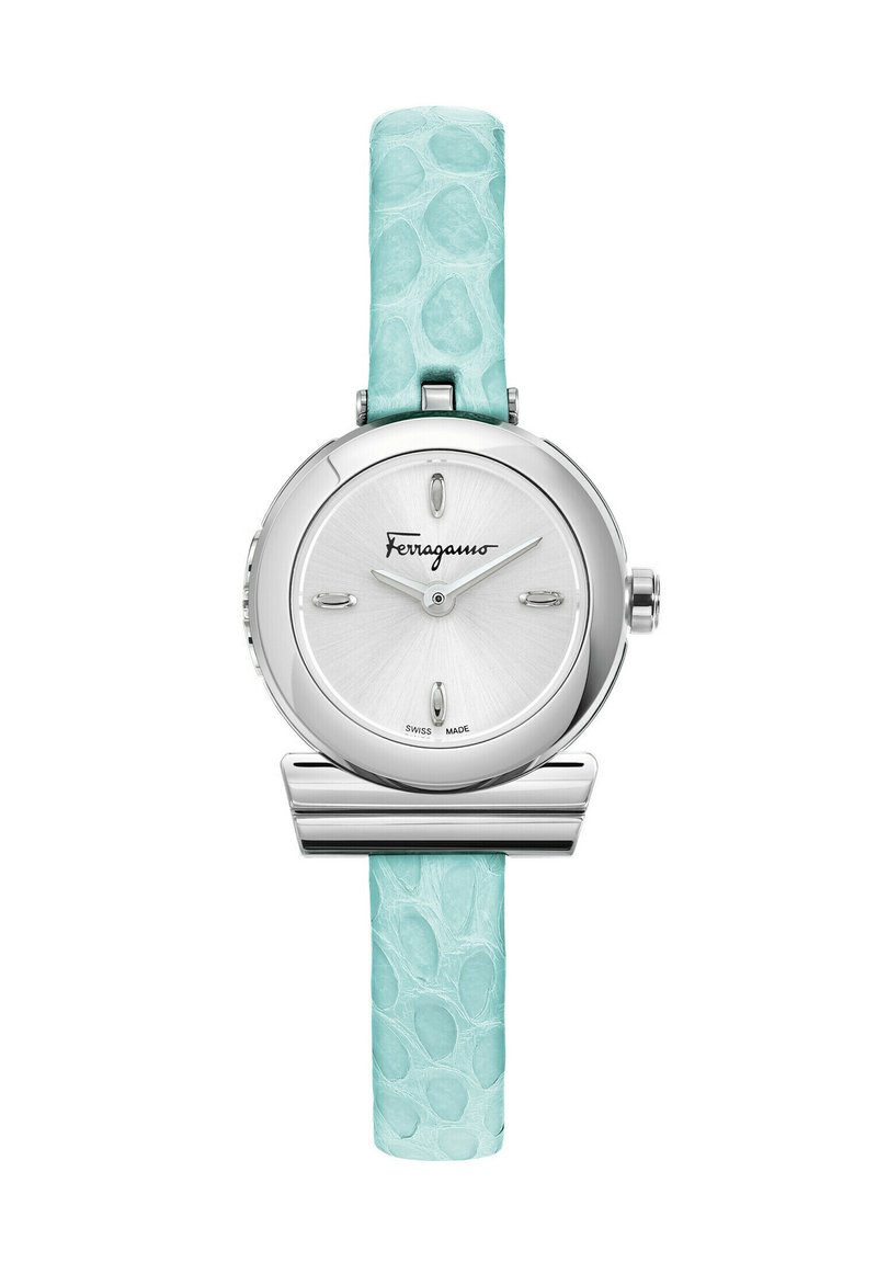 Kulaté stříbrné hodinky s texturovaným světle modrým koženým řemínkem. Bílý ciferník se stříbrnými akcenty a minimalistickým designem. Značka Ferragamo je zobrazená.