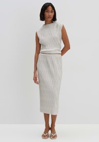 Grijze, geribbelde tweedelige outfit bestaande uit een mouwloos topje en een midi-rok, beiden met verticale texturen en een elastische tailleband. Zilveren sandalen.