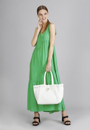 Zelené maxi šaty bez rukávů s volány, bílá kabelka s rýhami a detailem loga a černé sandály na silném podpatku.
