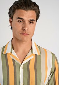 Camisa de manga corta con rayas verticales en amarillo, verde y beige. El material es suave con una textura agradable y un cuello clásico.