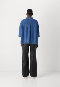 Blaues Denim-Jacket mit lockerer Passform, mit Kragen, Dreiviertelärmeln und einer schwarzen Lederhose, die einen geschichteten Look kreiert.