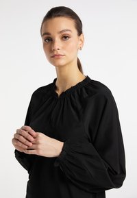 Mustat puserot, joissa on rypistetty kaula-aukko ja pullistuneet hihat. Silkka kangas, johon on lisätty joustavia yksityiskohtia hihojen helmassa ja hienovarainen kauluksen yksityiskohta.