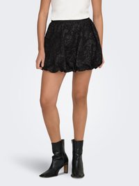 Zwarte kanten rok met geschulpte zoom, met een bloemmotief. Draagt zwarte leren enkellaarsjes en een aansluitend wit topje.