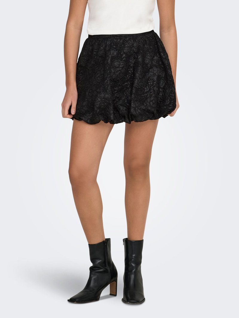 Zwarte kanten rok met geschulpte zoom, met een bloemmotief. Draagt zwarte leren enkellaarsjes en een aansluitend wit topje.