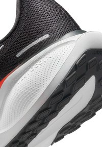 Chaussure de sport noire avec tige en mesh, présentant une semelle intermédiaire blanche texturée et une semelle extérieure en caoutchouc noir avec un motif de semelle anguleux. Détail d'accent rouge.