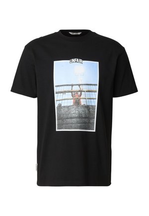 Czarny t-shirt z grafiką osoby stojącej za ogrodzeniem, trzymającej się za pręty, a nad obrazem napis "NIESPRAWIEDLIWE".